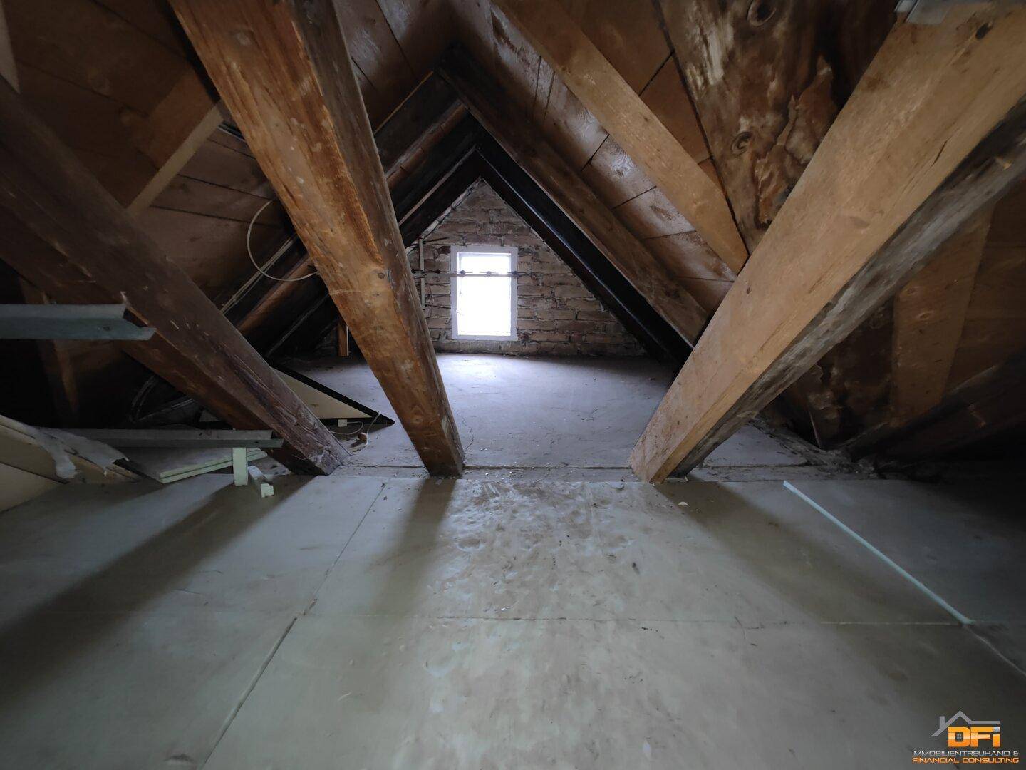 Geräumiger Dachboden mit sichtbaren Holzbalken und kleinem Fenster, bereit für den Ausbau.