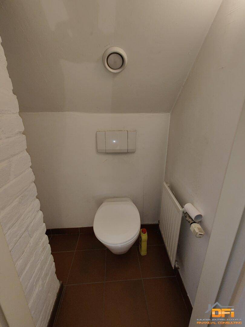 Kleines Gäste-WC mit Wand-WC, Heizkörper und Lüftung in schräger Dachschräge.