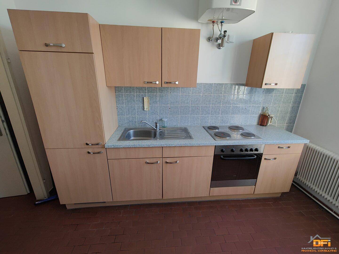 Einbauküche mit hellen Holzfronten, integriertem Herd und Spüle, ergänzt durch einen Warmwasserboiler.