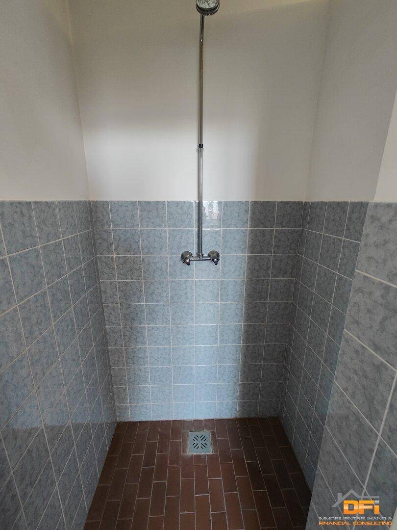 Duschbereich mit grauen Wandfliesen und Terrakotta-Boden, ausgestattet mit einer einfachen Duscharmatur.