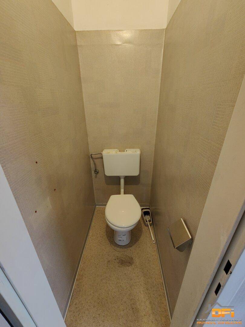 Schmale Toilette mit Spülkasten und Toilettenbürste, in einem gut gepflegten Zustand.