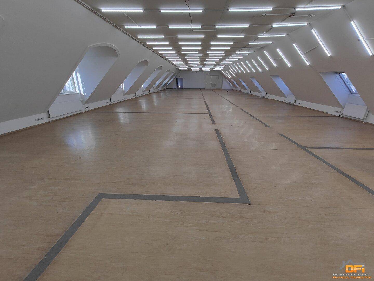 Geräumiger Dachgeschossraum mit vielen Fenstern, Schrägen und effizienter Deckenbeleuchtung.