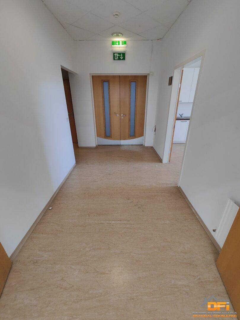 Heller Flur mit Holztüren, einem Ausgangsschild und Blick in eine kleine Küche.