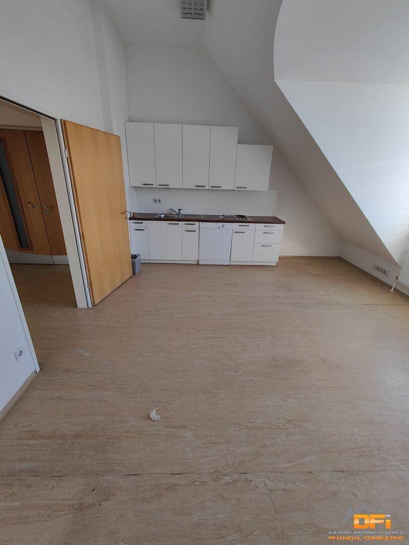 Kleine Küchenzeile mit weißen Schränken und Geräten in einem Raum mit Dachschräge.