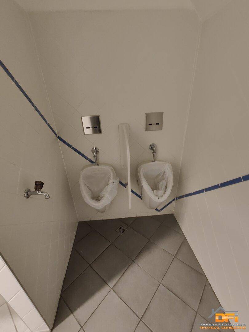 Zwei Urinale in einem gefliesten Toilettenraum mit blauen Akzentstreifen.