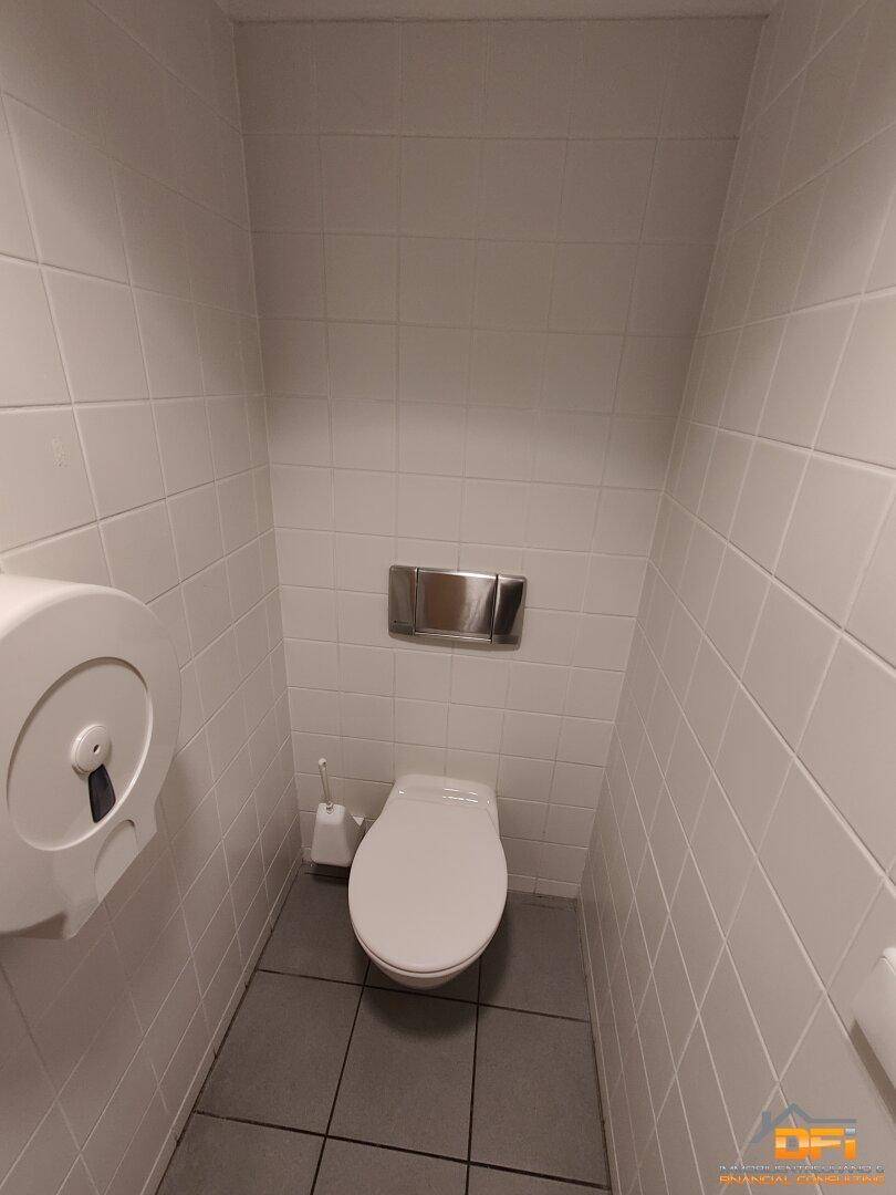 Toilettenkabine mit Wand-WC und weiß gefliesten Wänden.