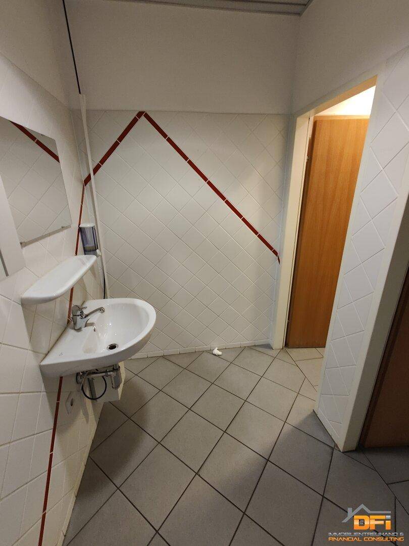 Waschbereich in einer öffentlichen Toilette mit Waschbecken und rot akzentuierten Fliesen.