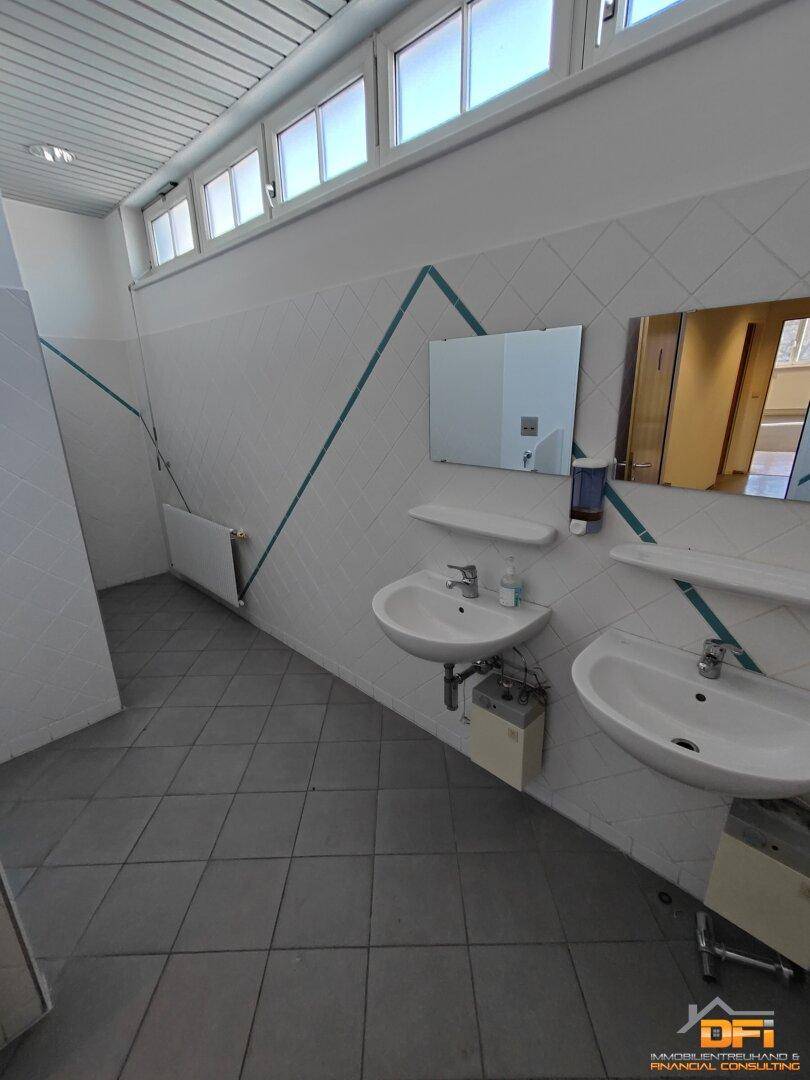Funktionaler Waschraum mit zwei Waschbecken, Spiegeln, gefliesten Wänden und kleinen Oberlichtern.