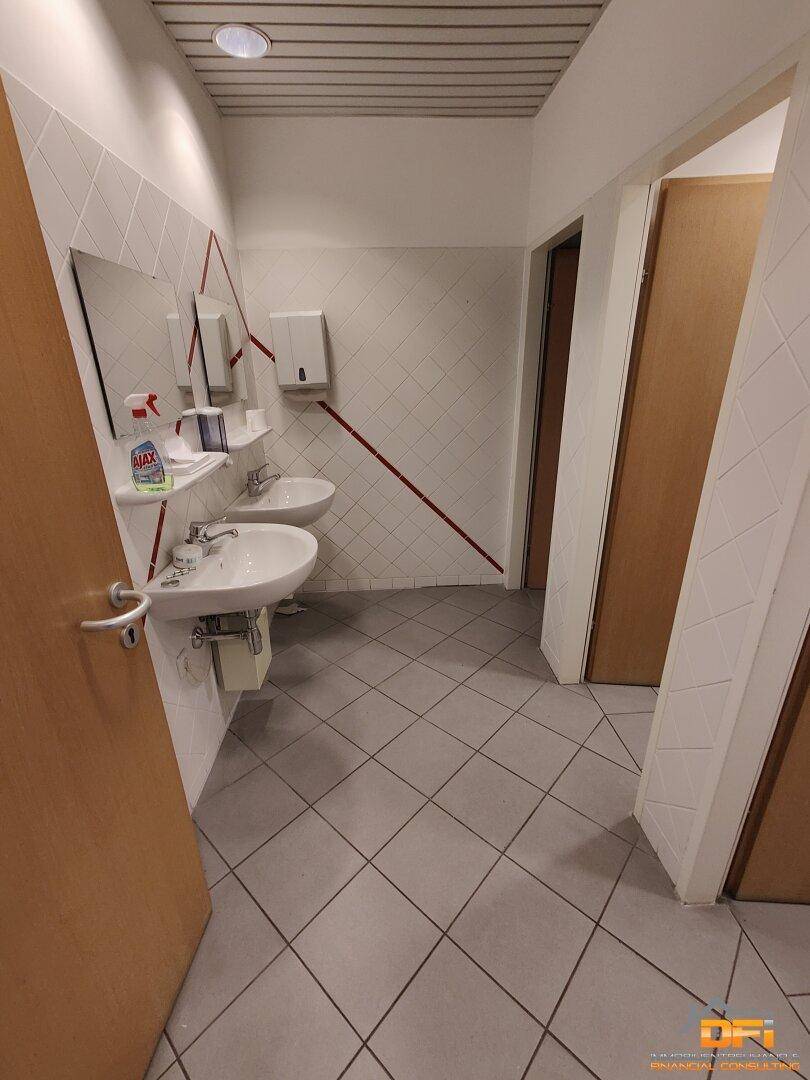 Badezimmer mit mehreren Waschbecken, Spiegeln und gefliesten Wänden, akzentuiert durch einen roten Streifen.