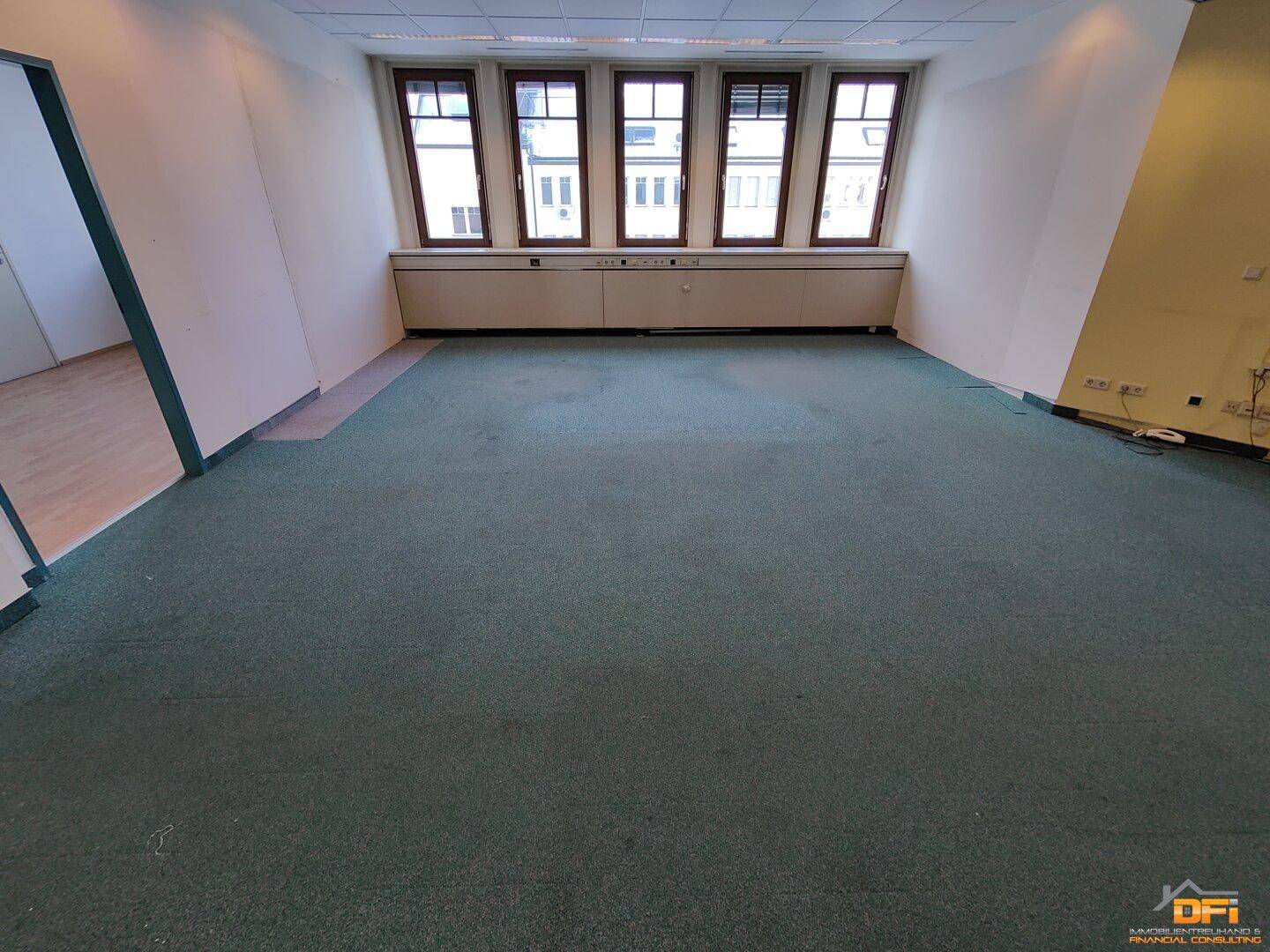 Bürofläche mit grünem Teppichboden und einer Reihe von Fenstern, die Tageslicht hereinlassen.
