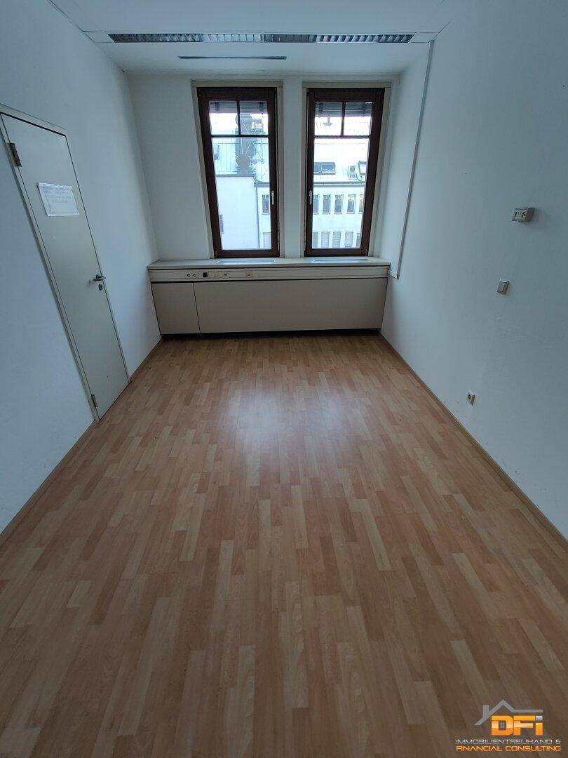 Kleines Büro mit hellem Laminatboden und zwei Fenstern, die eine angenehme Arbeitsatmosphäre schaffen.