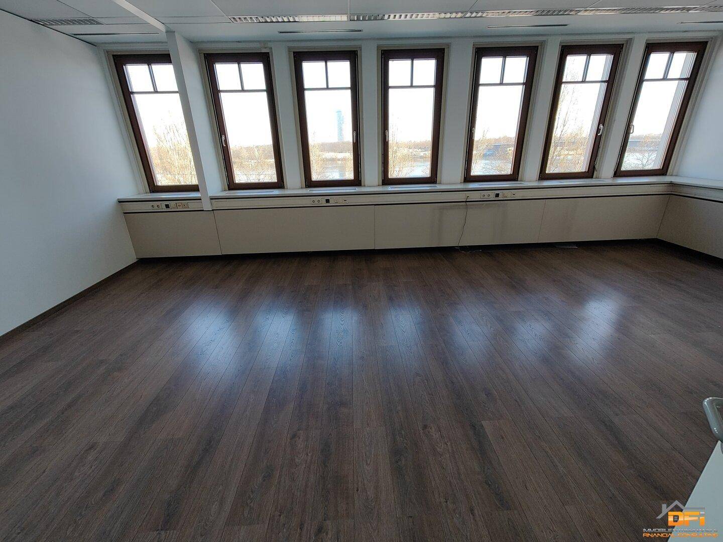 Großes Büro mit dunklem Laminatboden und schrägen Fenstern, die viel Licht bieten und eine weite Aussicht ermöglichen.