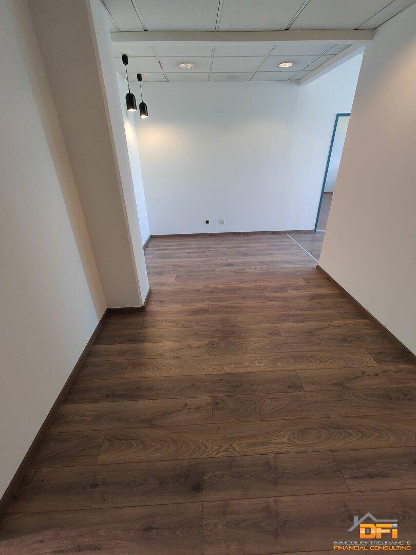 Heller Flur mit Laminatboden und modernen Deckenleuchten, der zu weiteren Büroräumen führt.