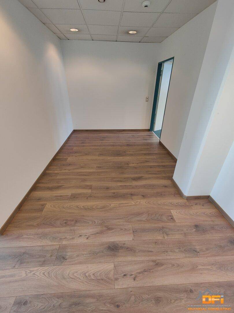 Schmaler Flur mit Laminatboden und weiß gestrichenen Wänden, der einen Durchgang zu anderen Bereichen bildet.