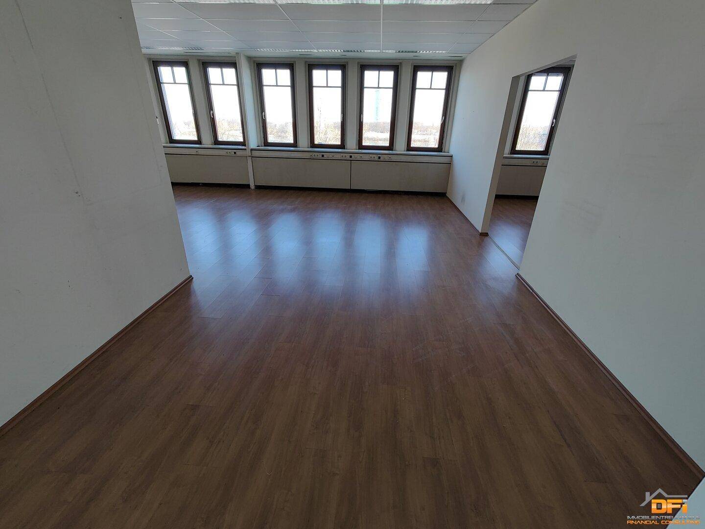 Geräumiges Büro mit hellem Laminatboden, vielen Fenstern und natürlichem Lichteinfall, ideal für Arbeitsplätze.