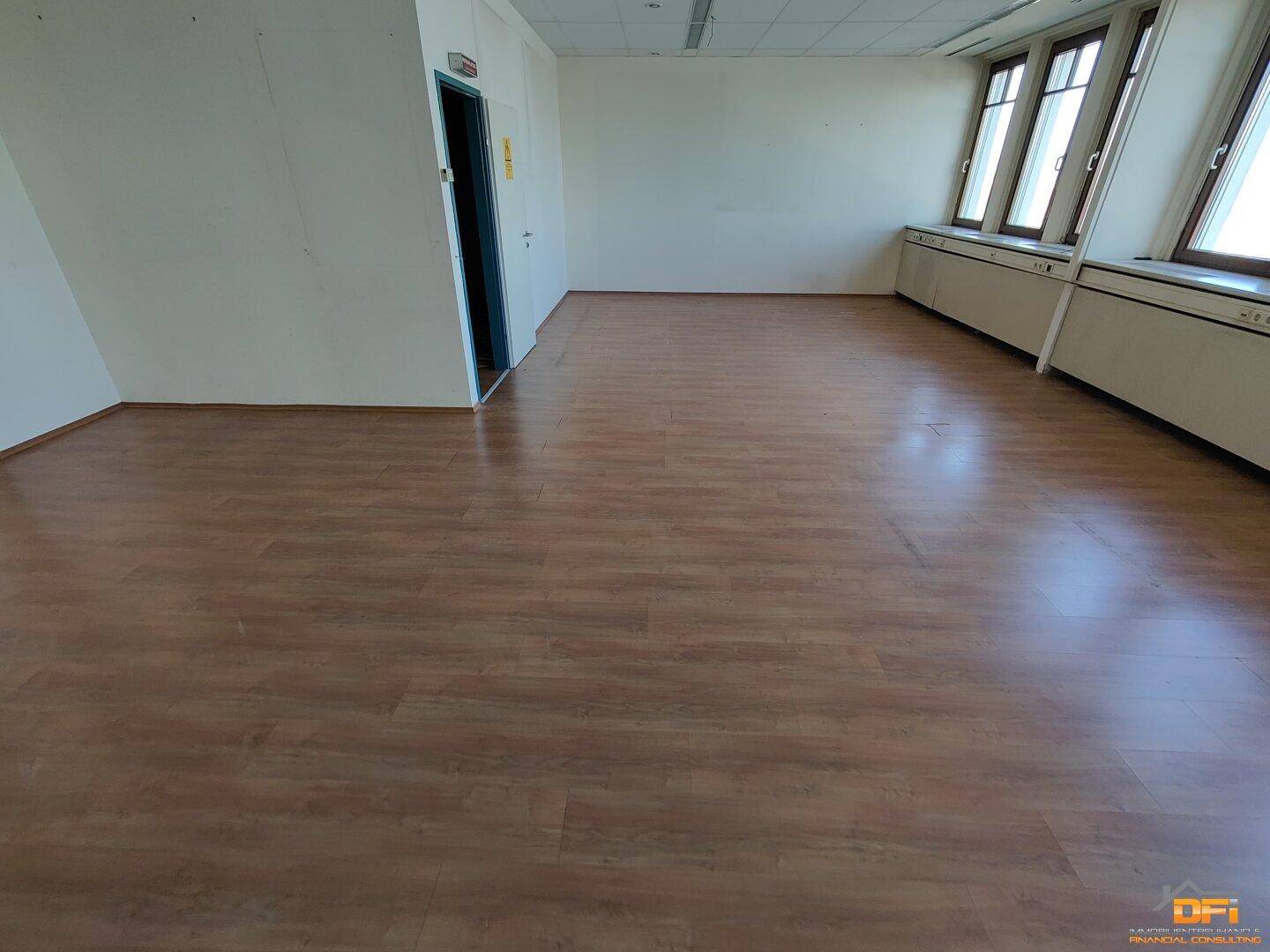 Helles Büro mit Laminatboden und Fensterfront, die den Raum mit Tageslicht durchflutet und eine Aussicht bietet.
