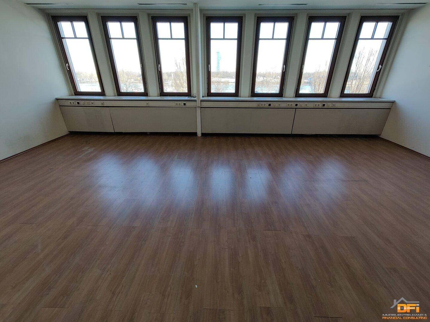 Großes Büro mit hellem Laminatboden und einer langen Reihe von Fenstern mit weitem Ausblick.