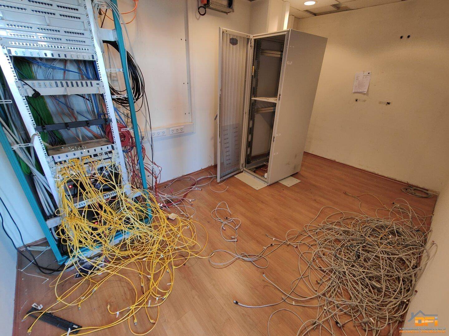 Serverraum mit umfangreicher Verkabelung und einem leeren Serverschrank, bereit für die Installation von Technik.