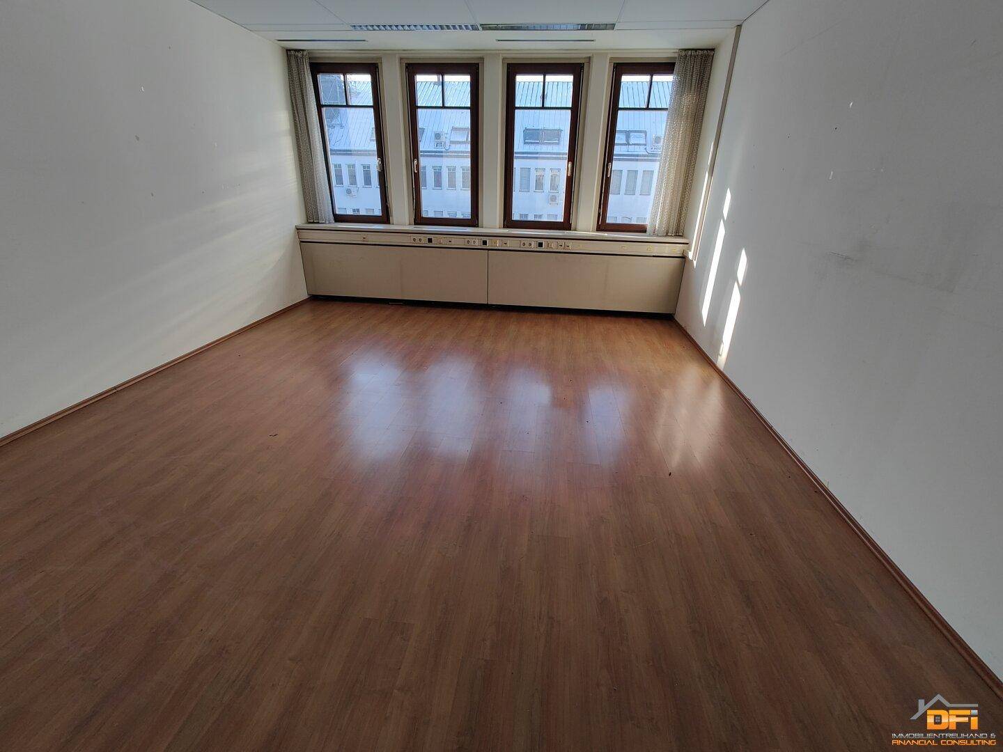 Büro mit hellem Laminatboden und Fenstern, die den Raum mit Sonnenlicht durchfluten und Stadtblick bieten.