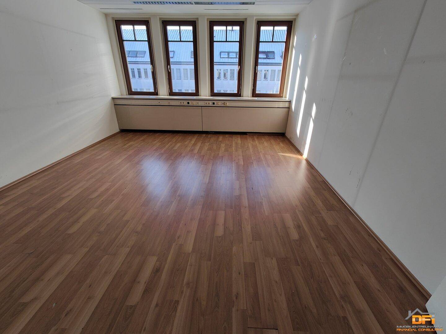 Helles Büro mit Laminatboden und Fenstern, die viel Tageslicht in den Raum lassen und Stadtblick bieten.