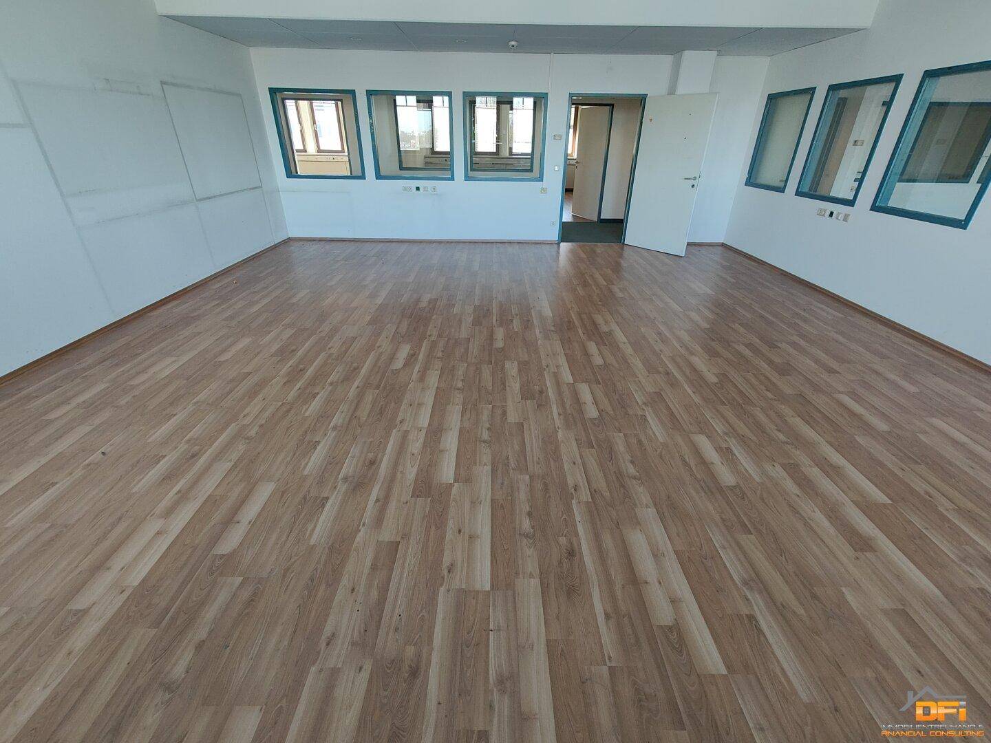 Geräumiges Büro mit hellem Laminatboden und mehreren Fenstern, die den Raum erhellen und eine Aussicht bieten.