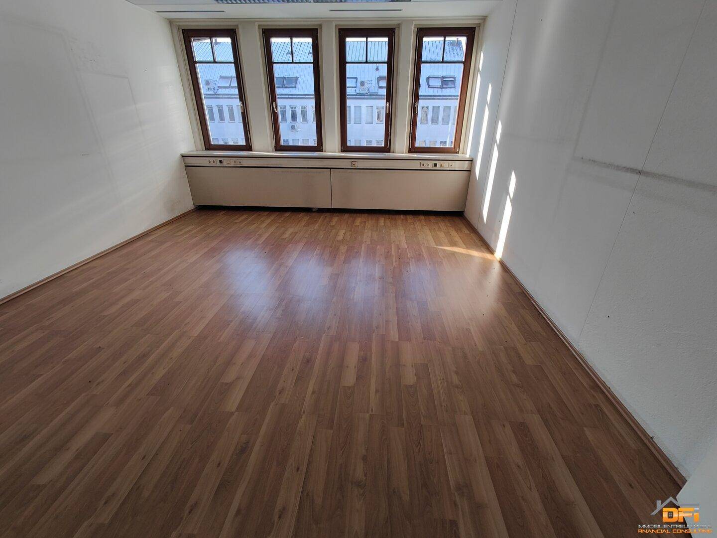 Büro mit hellem Laminatboden und Fenstern, die den Raum mit Sonnenlicht durchfluten und Stadtblick bieten.