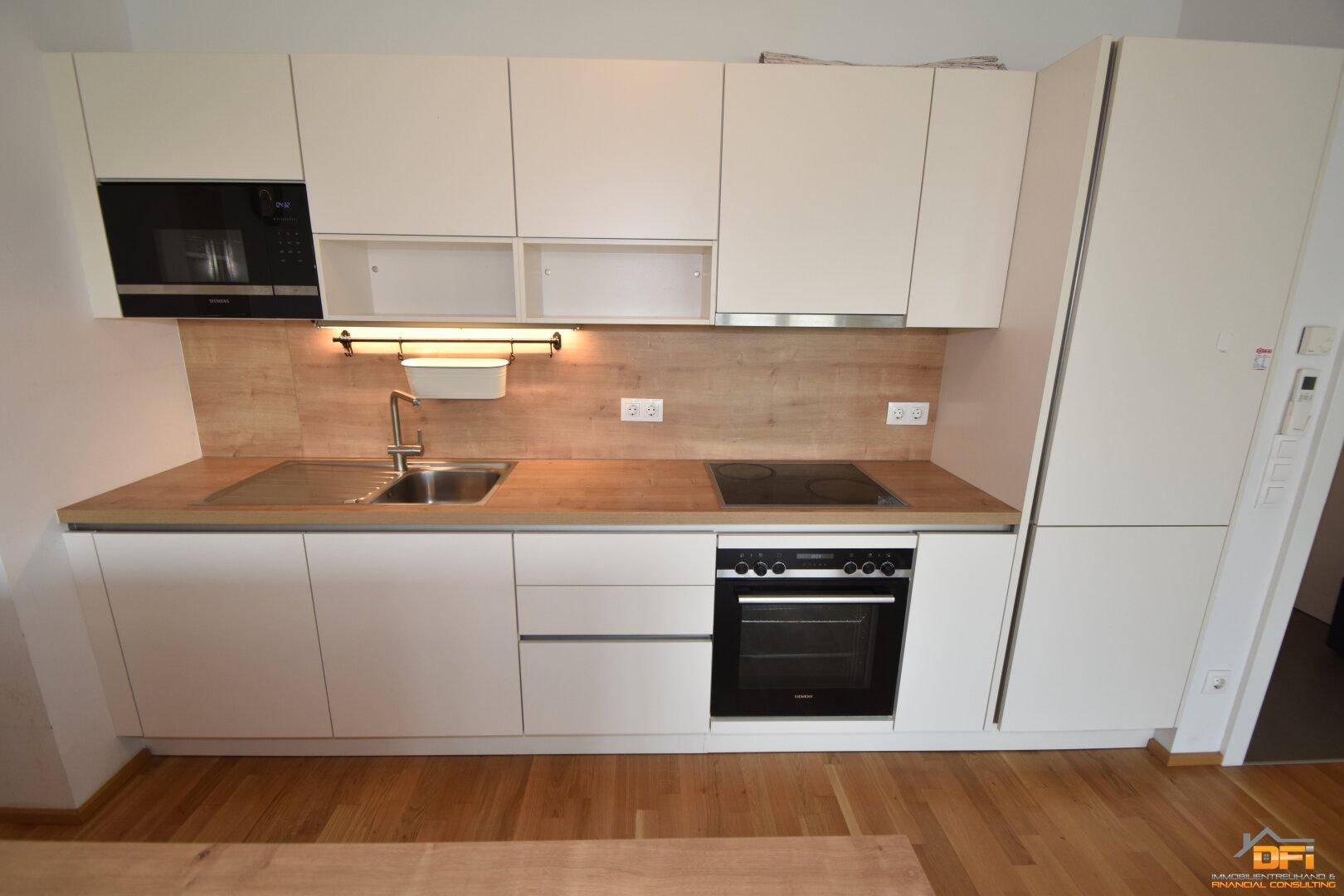Moderne Einbauküche mit weißen Schränken, Holz-Arbeitsplatte und integrierten Elektrogeräten.