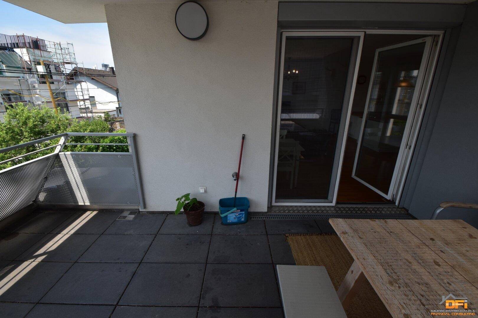 Heller Balkon mit Fliesenboden und Schiebetürzugang vom Innenbereich, bietet einen Blick ins Grüne.