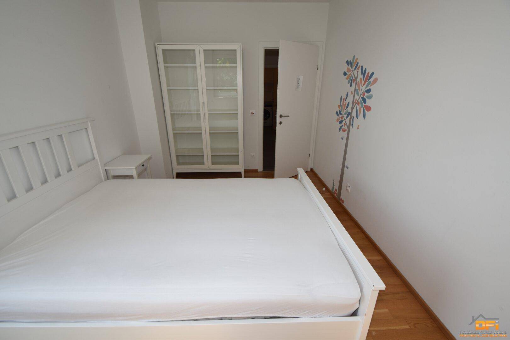Schlafzimmer mit Holzboden, weißem Bett und einem weißen Schrank, bietet eine ruhige Atmosphäre.
