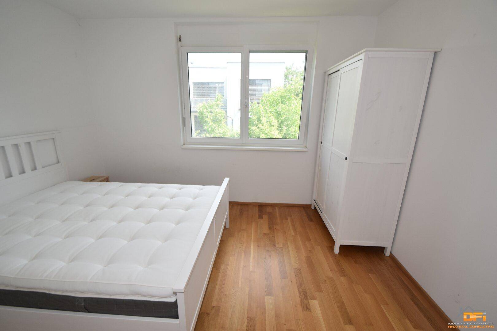 Helles Schlafzimmer mit Holzboden, weißem Bett und Kleiderschrank, mit Blick auf die Umgebung.