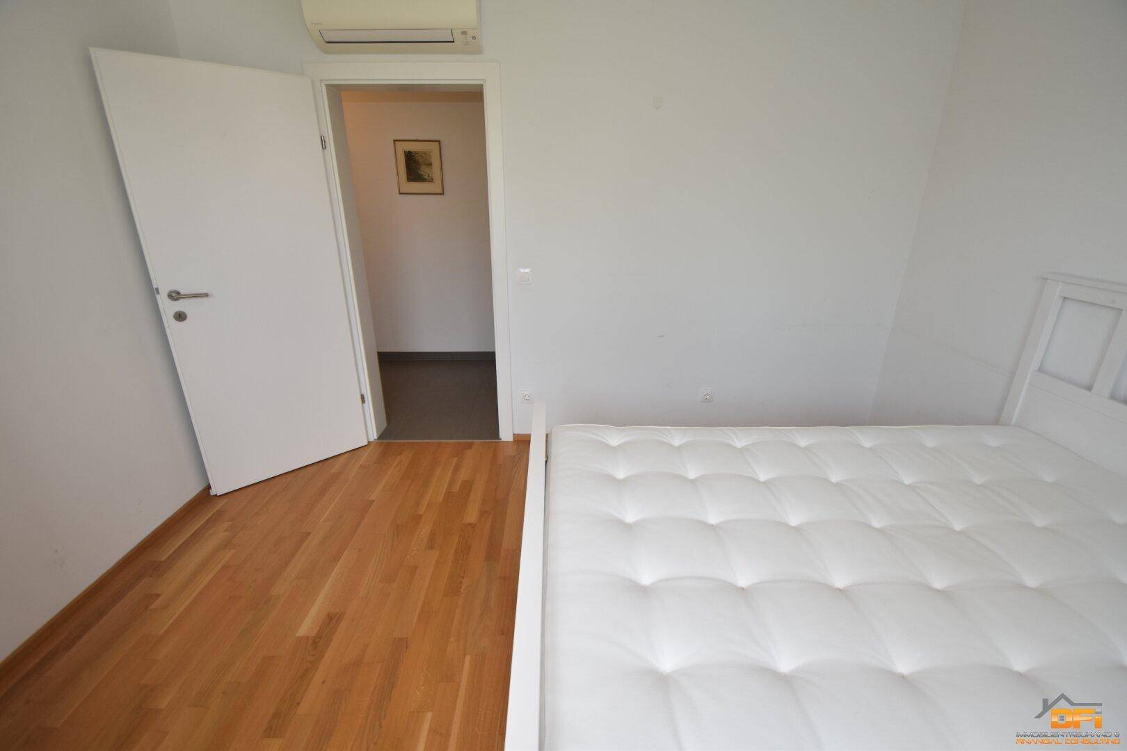 Schlafzimmer mit Holzboden und weißem Bett, bietet Zugang zum Flur und ist mit Klimaanlage ausgestattet.