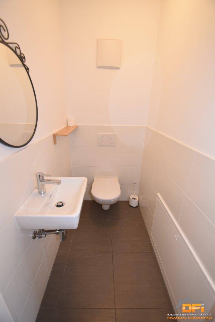 Modernes Gäste-WC mit Fliesenboden, wandhängendem WC und kleinem Waschbecken.