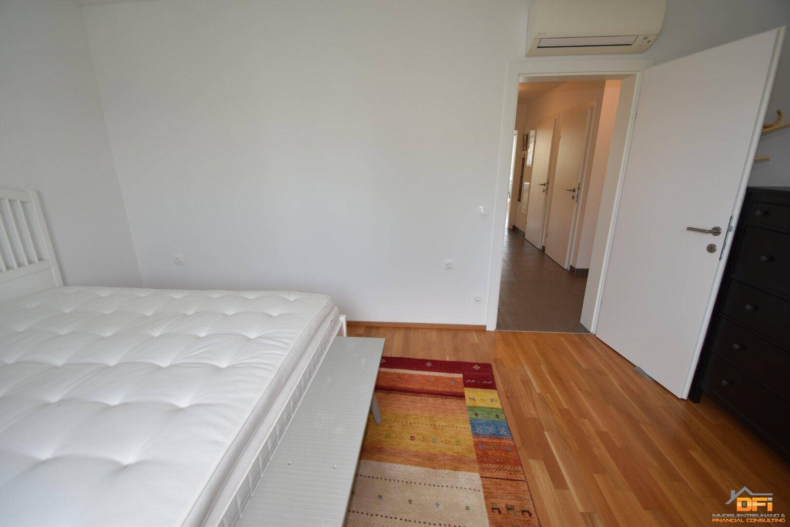 Schlafzimmer mit Holzboden und weißem Bett, bietet Zugang zum Flur und ist klimatisiert.