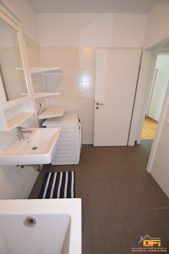 Badezimmer mit Fliesenboden, Waschbecken, Waschmaschine und Spiegelschrank, praktisch eingerichtet.