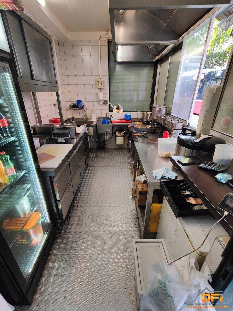 Schmale Gewerbeküche im Imbissstand mit Edelstahltheken, Fliesenwänden und professionellen Geräten.