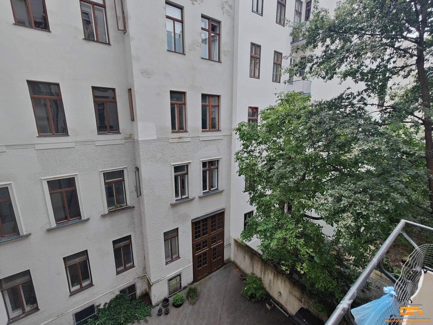 Innenhof eines Altbaus mit Bäumen und Blick auf die umliegenden Fenster.