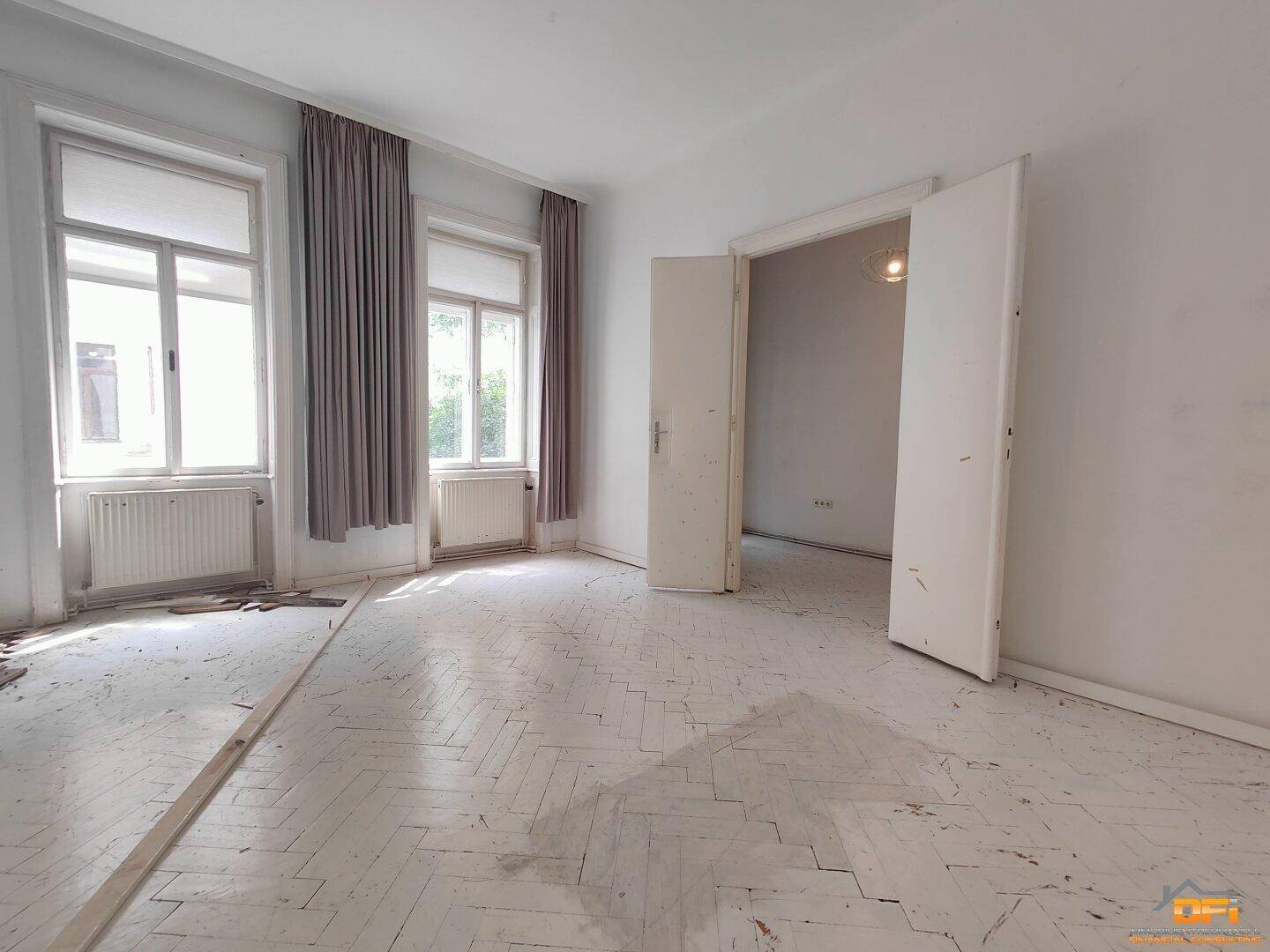 Geräumiger Raum mit Fischgrätparkett und hohen Fenstern, ideal für Schlaf- oder Wohnzimmer.