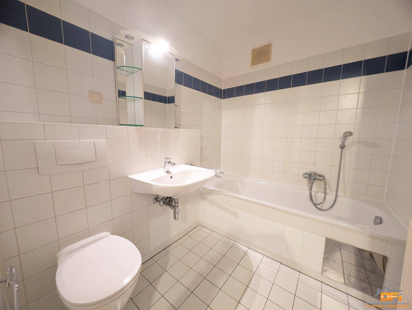 Funktionales Badezimmer mit Badewanne, WC und Waschbecken, ausgestattet mit weißen Fliesen und blauen Akzenten.
