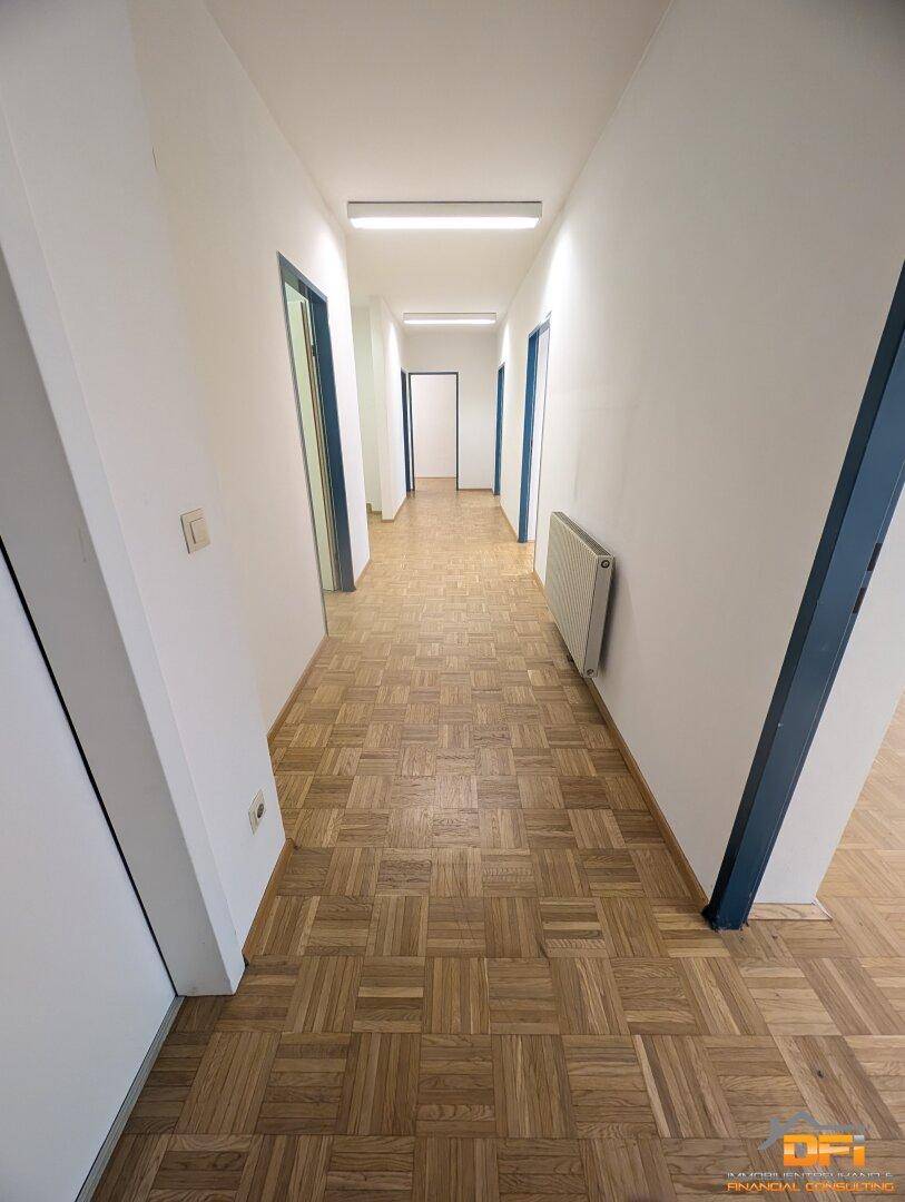 Langer Flur mit Parkettboden und mehreren Türen, der verschiedene Büroräume verbindet.