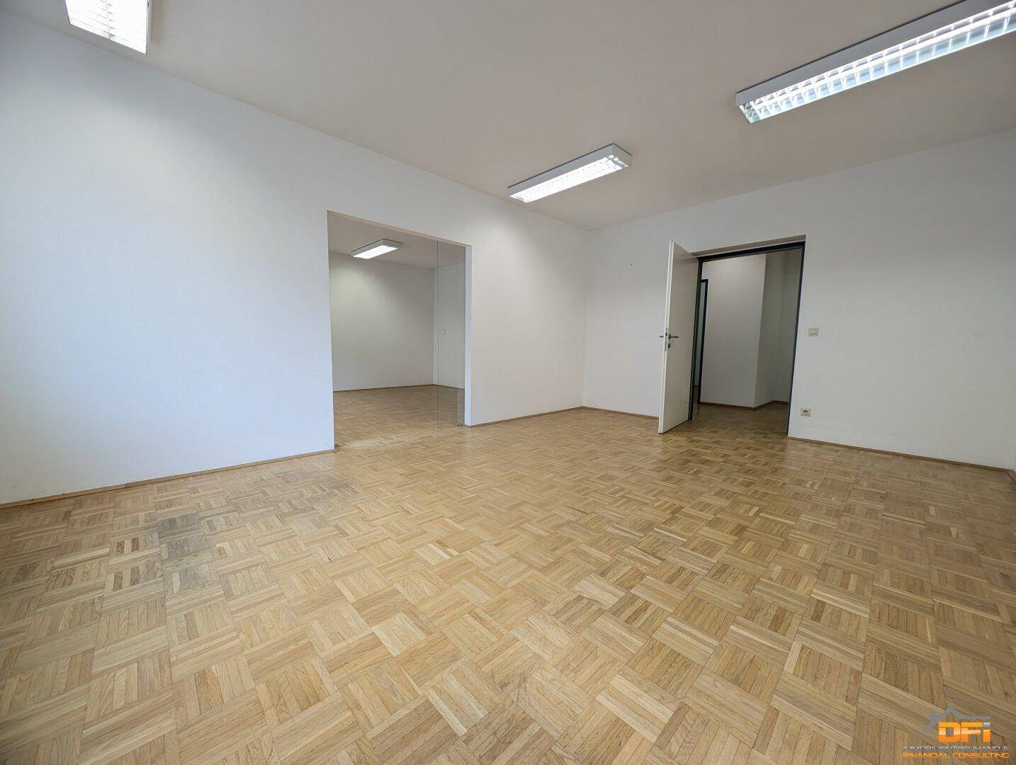 Großes, leeres Büro mit Parkettboden und mehreren Zugängen zu angrenzenden Räumen.