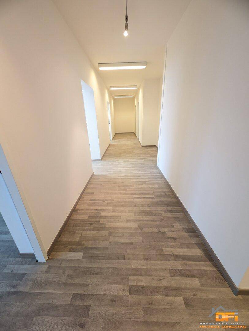 Langer, heller Flur mit Holzoptikboden und mehreren Deckenleuchten, der zu weiteren Räumen führt.