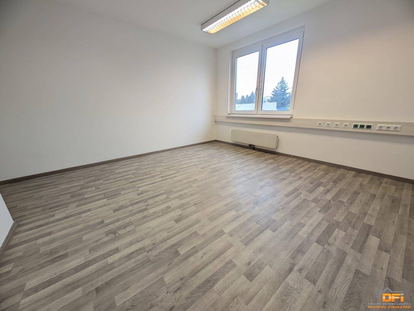Heller Büroraum mit Holzoptikboden, großen Fenstern und Deckenleuchten, bietet viel Tageslicht.