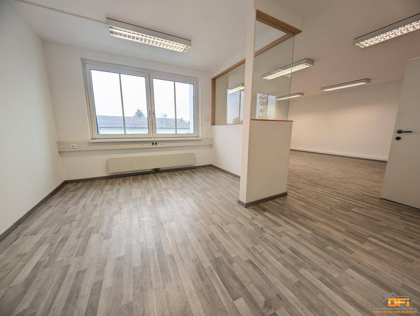 Großzügiger Bürobereich mit Holzoptikboden, großen Fenstern und einer Raumteilung für flexible Nutzung.
