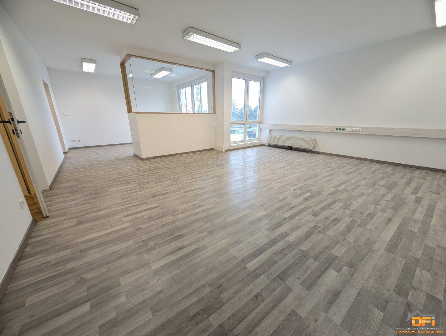 Geräumiger Bürobereich mit Holzoptikboden, großen Fenstern und einer Raumteilung für flexible Nutzung.