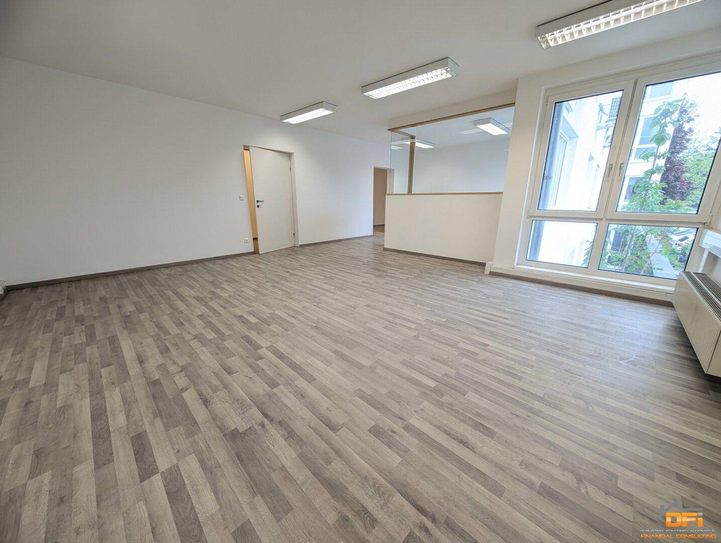 Heller und offener Büroraum mit Holzoptikboden, großen Fenstern und viel natürlichem Licht.