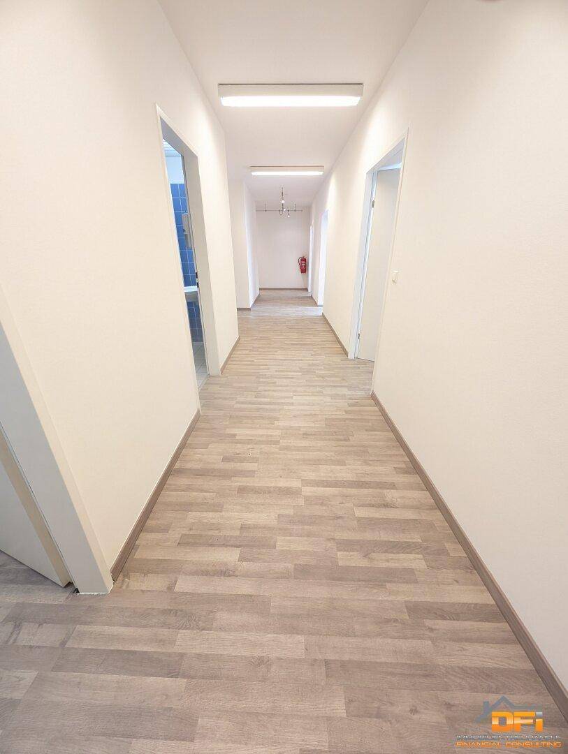 Langer, heller Flur mit Holzoptikboden und effizienter Deckenbeleuchtung, der zu verschiedenen Räumen führt.