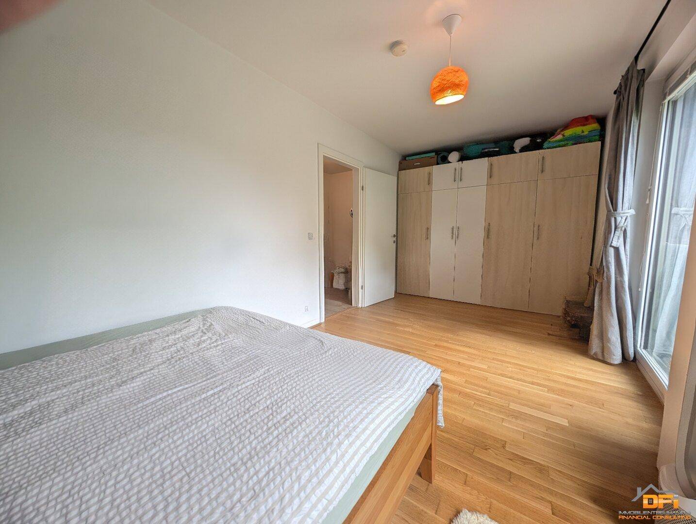 Schlafzimmer mit Holzboden, großem Kleiderschrank und Zugang zu einem angrenzenden Badezimmer.