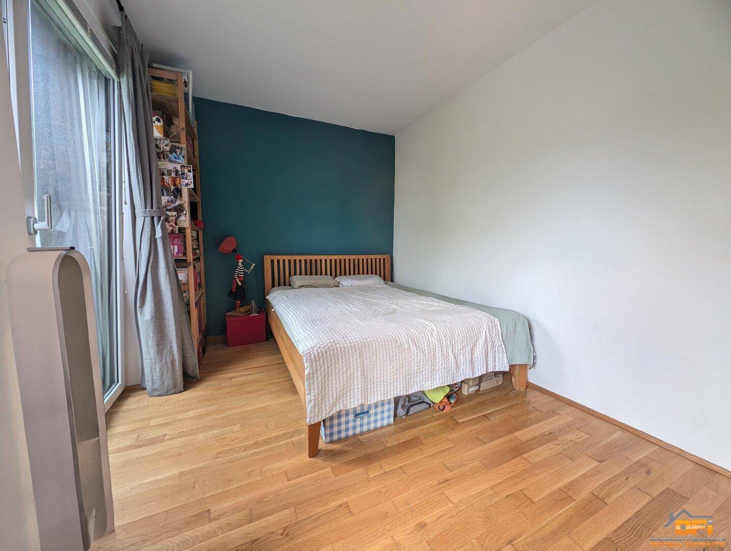 Helles Schlafzimmer mit Holzboden und einer auffälligen tealfarbenen Wand als Blickfang.
