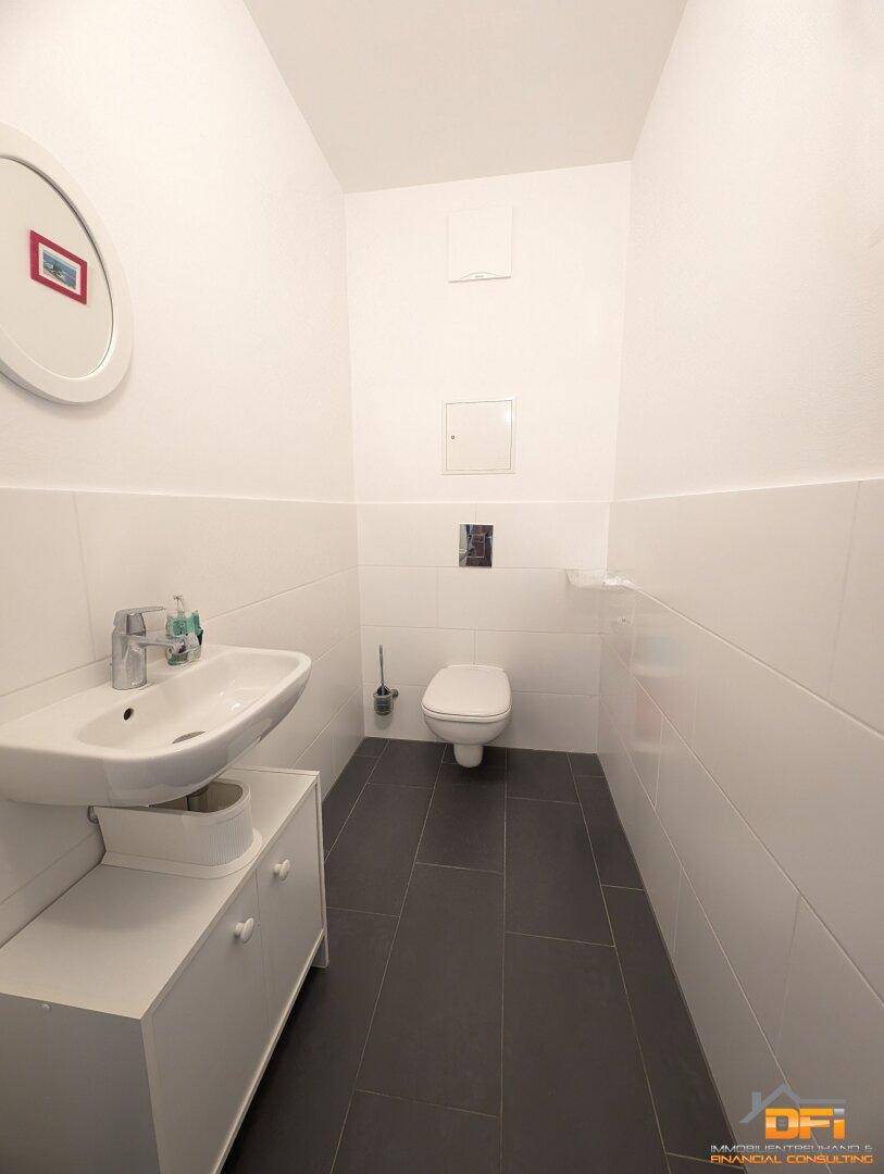 Separates Gäste-WC mit wandhängender Toilette, kleinem Waschbecken und dunklem Fliesenboden.