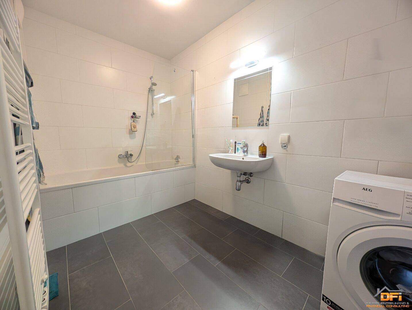 Modernes Badezimmer mit Badewanne, Dusche, Waschbecken und Waschmaschine.